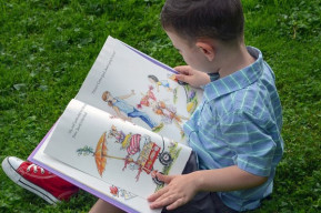 un bambino legge un libro seduto in un campo