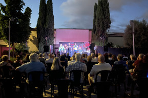 Foto a colori di uno spettacolo nel Giardino Elisabetta con gli attori in piedi sul palco e il pubblico seduto